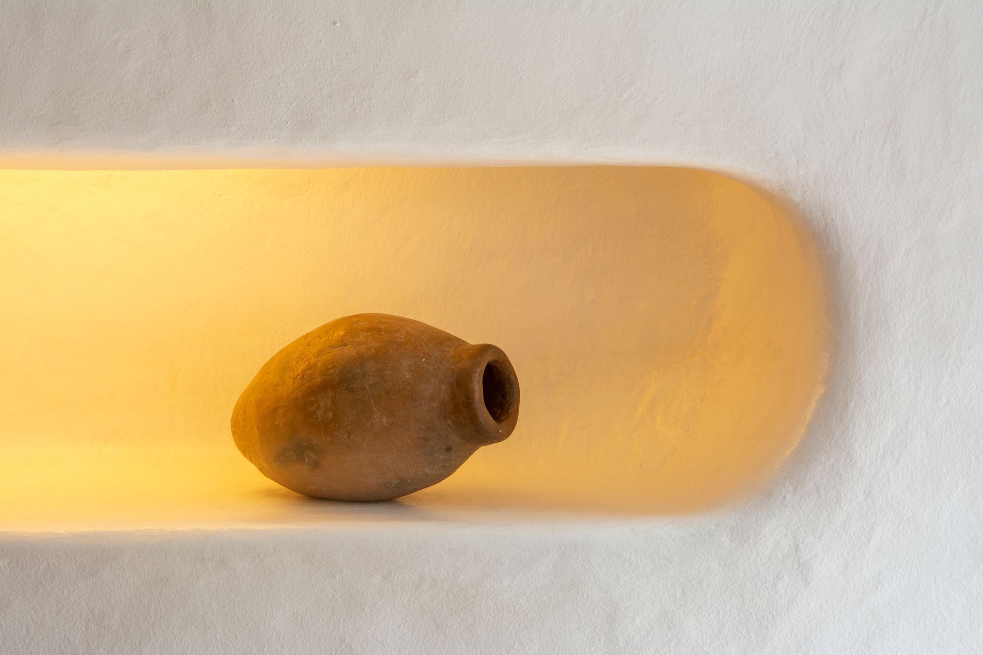 A rustic clay jar displayed in a niche with warm lighting, showcasing ancient pottery.