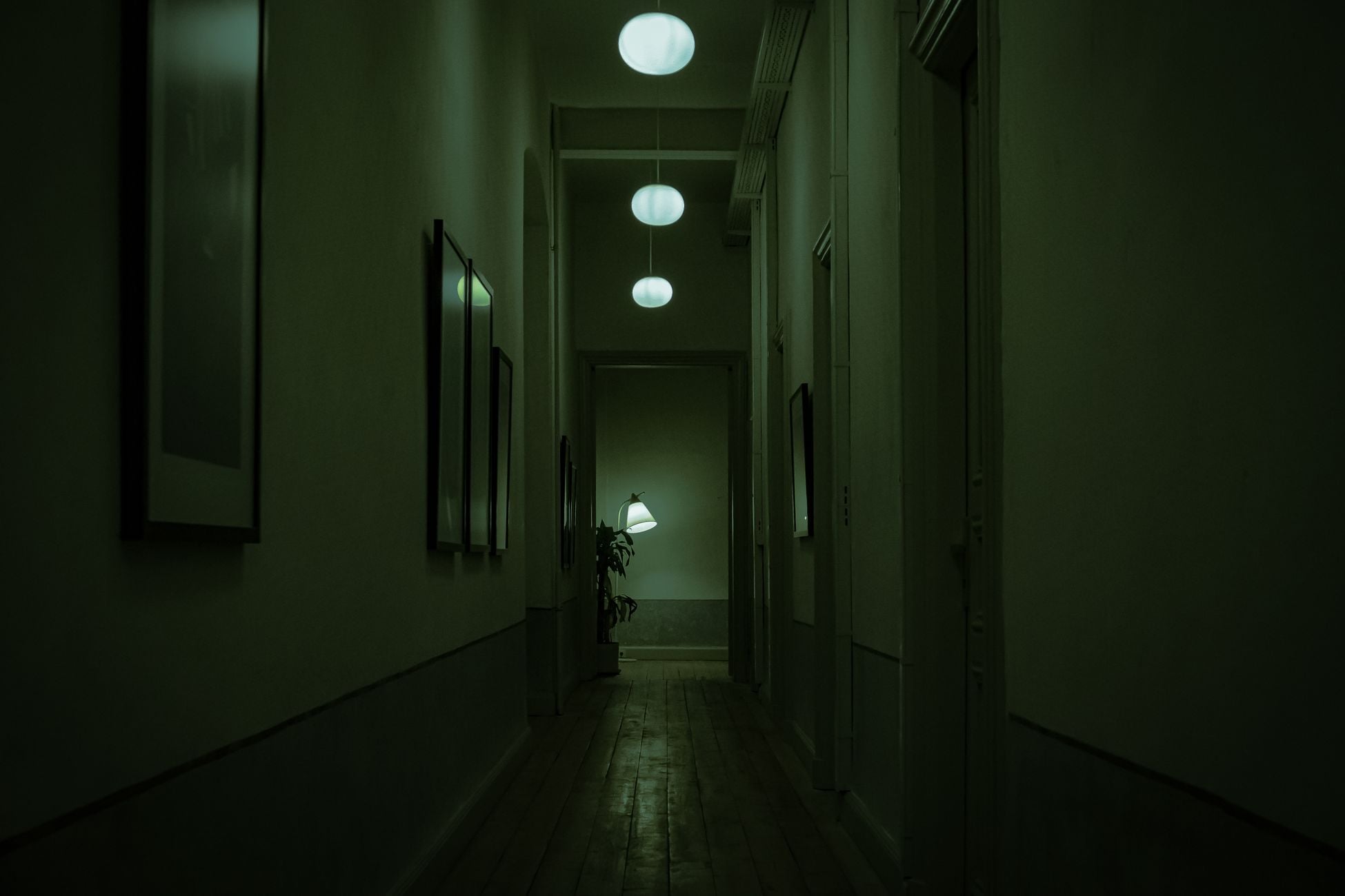 Explore the moody atmosphere of a narrow corridor with green lighting and hanging lamps.