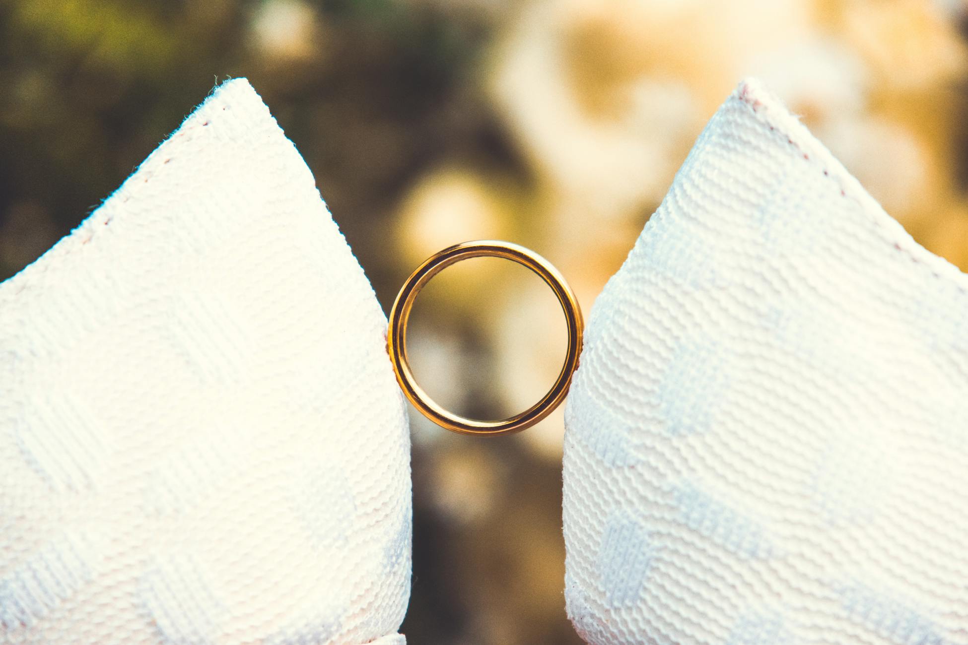 A close-up of a gold wedding ring placed on textured white fabric with a soft background.