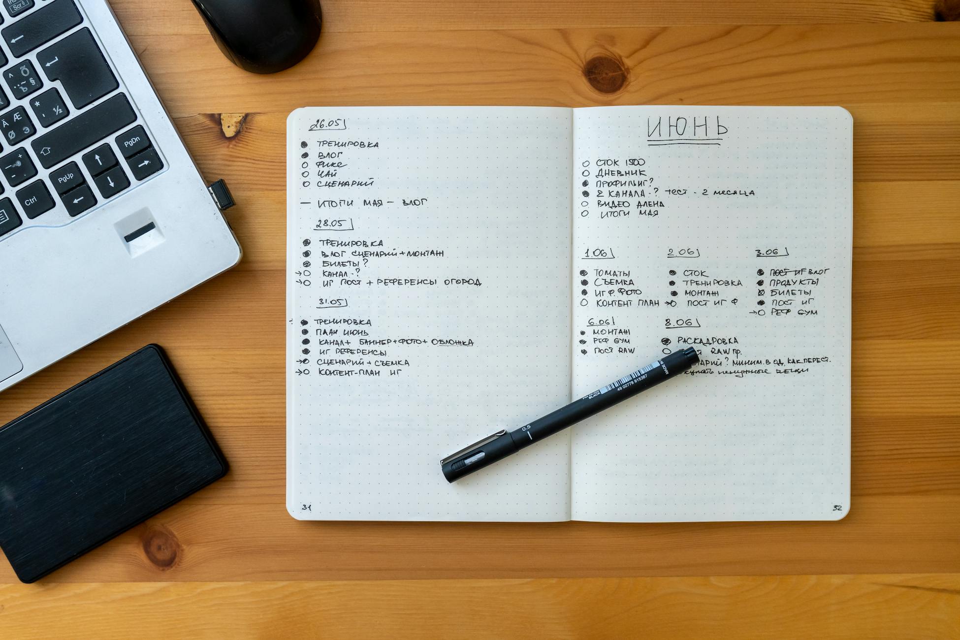 Top view of a workspace featuring a laptop, an open notebook with handwritten notes, and a pen.