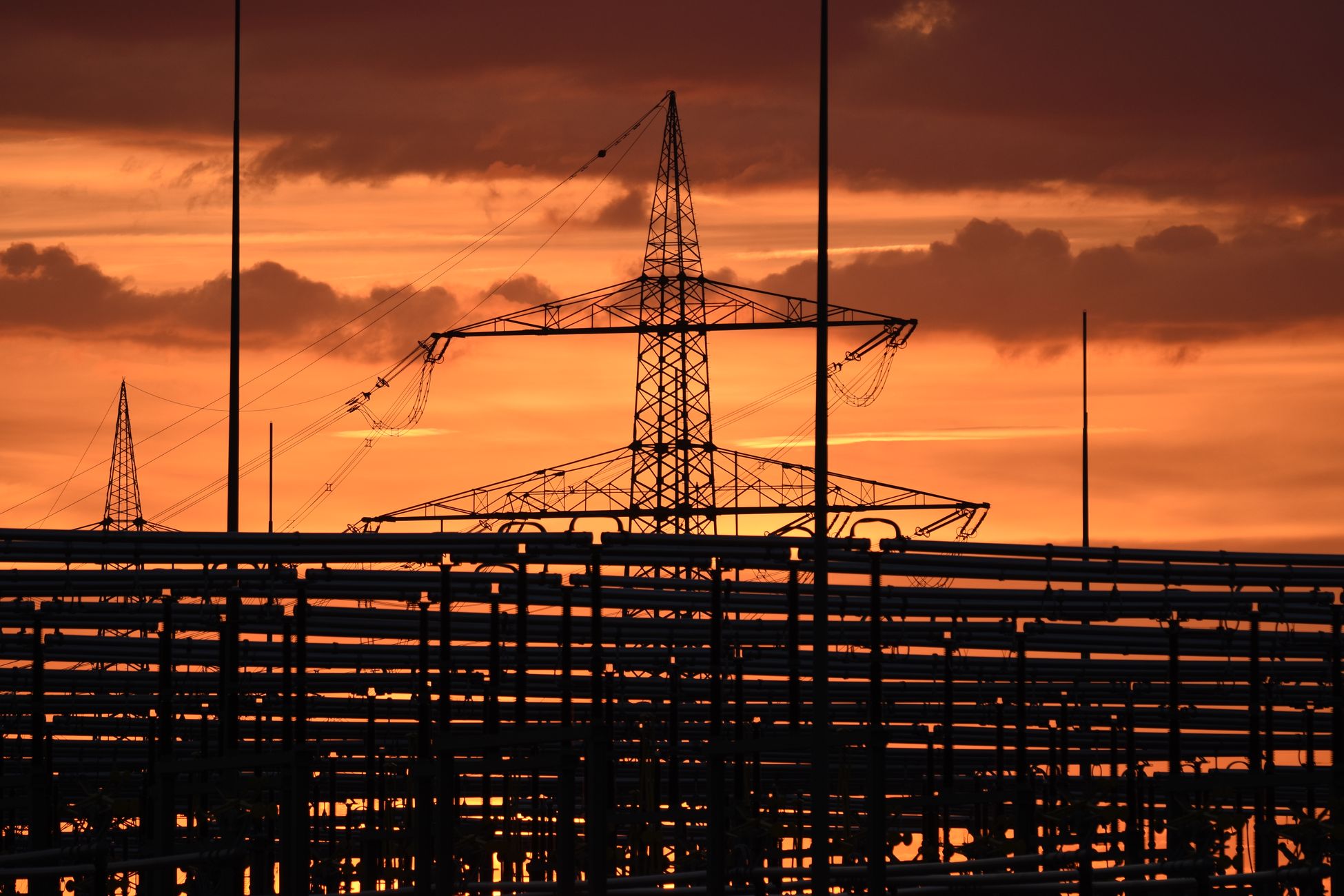 Silhouetted electric tower against vivid sunset sky, highlighting urban infrastructure.