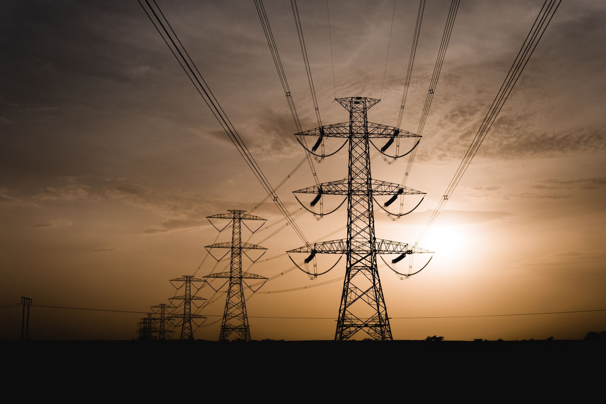 Silhouetted power lines stretch across the landscape at sunset, capturing electric tranquility.