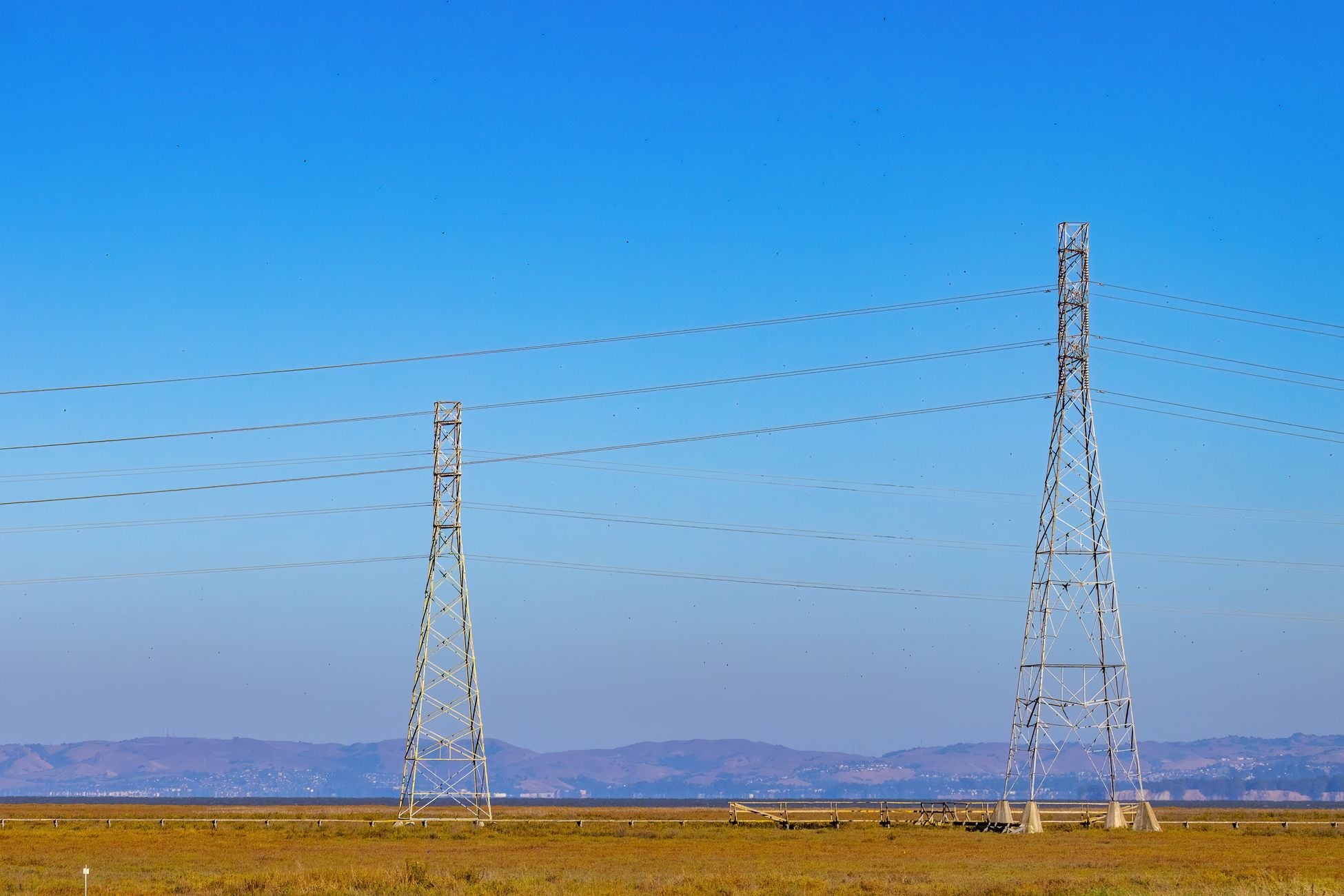 Electric towers and power lines under a clear blue sky in a natural landscape.