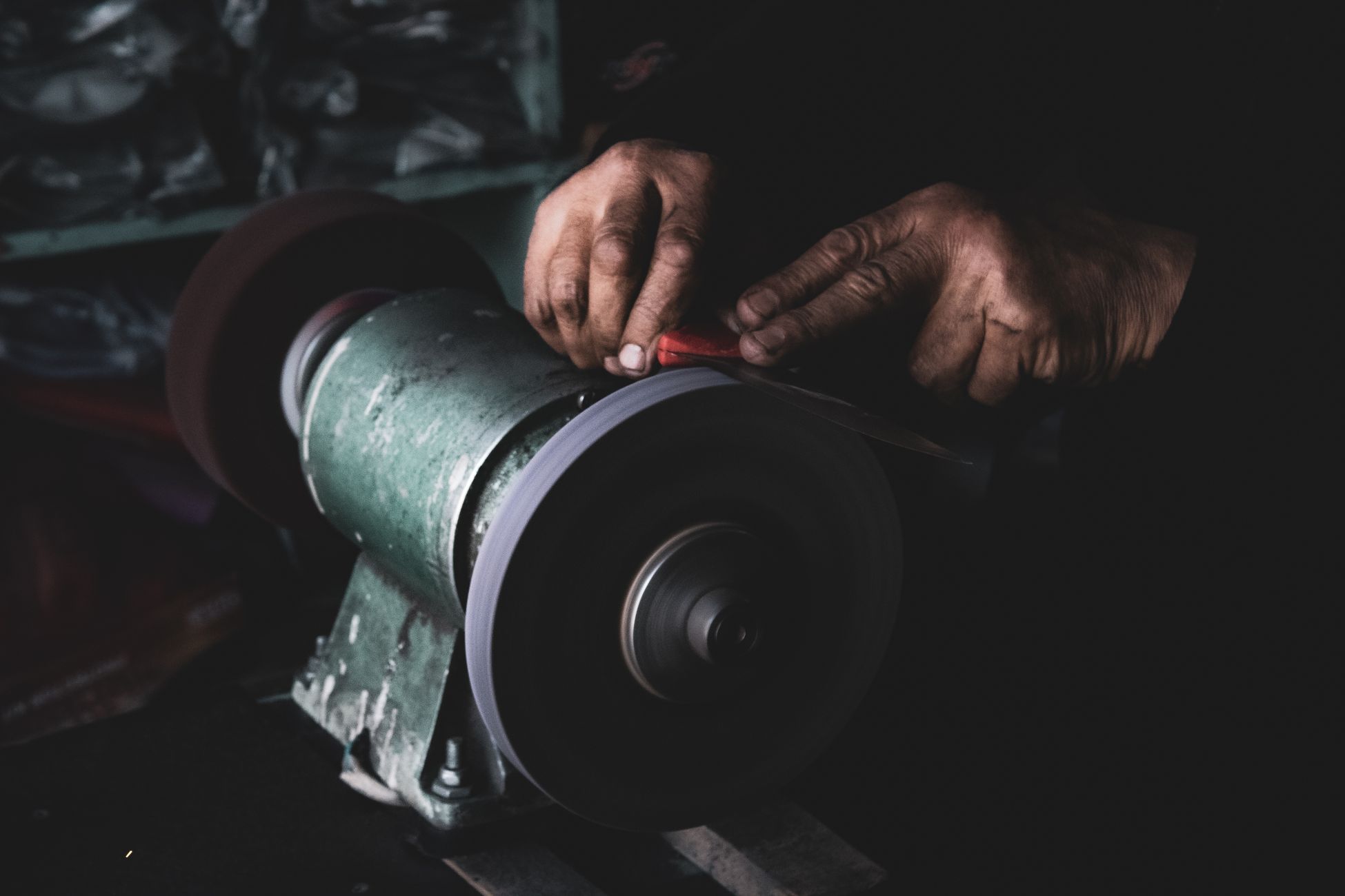 Detailed shot of hands carefully sharpening a blade using an electric grinder in a dimly lit workshop.