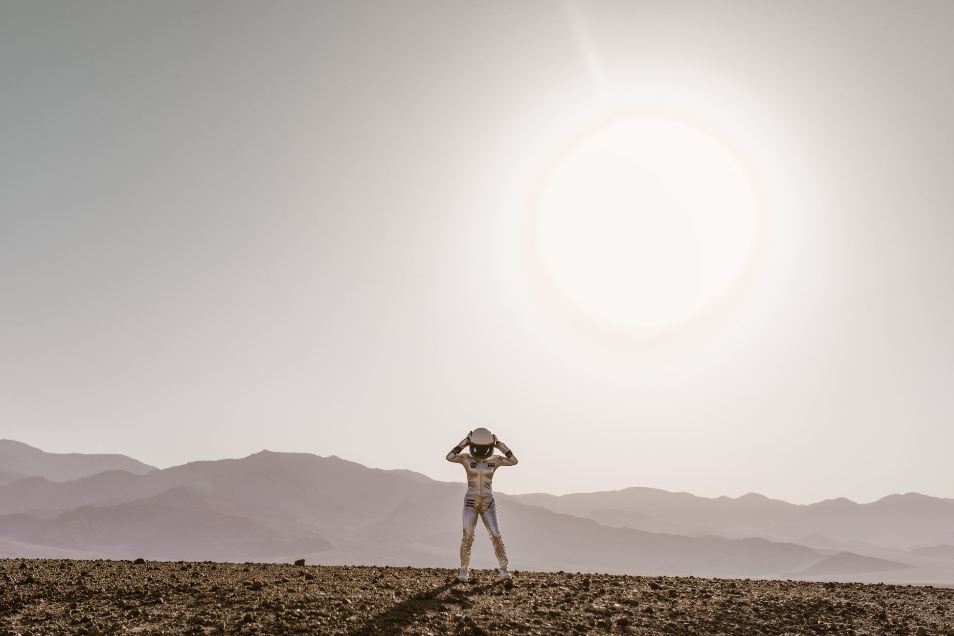 Astronaut in space suit stands under a bright sun in a barren desert landscape, evoking a sci-fi atmosphere.