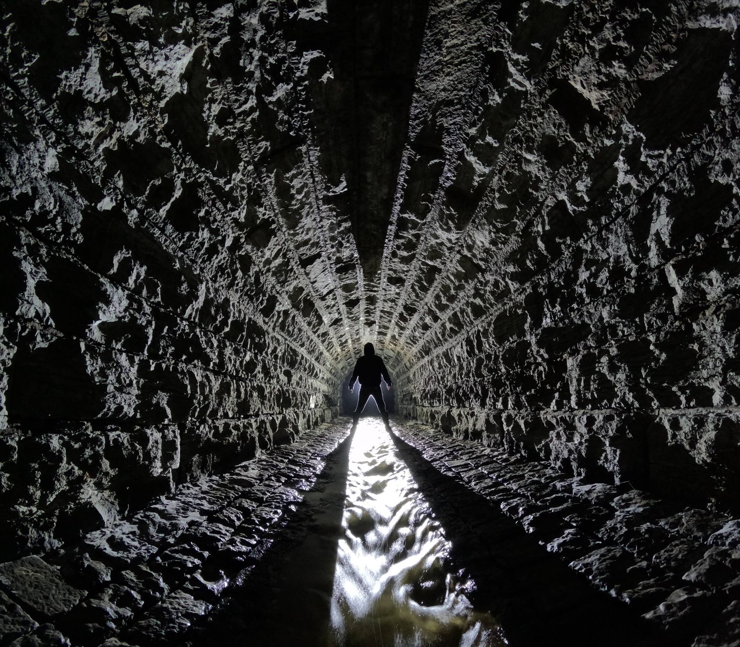 Silhouette of person in a dramatic stone tunnel, enhanced by bold lighting.