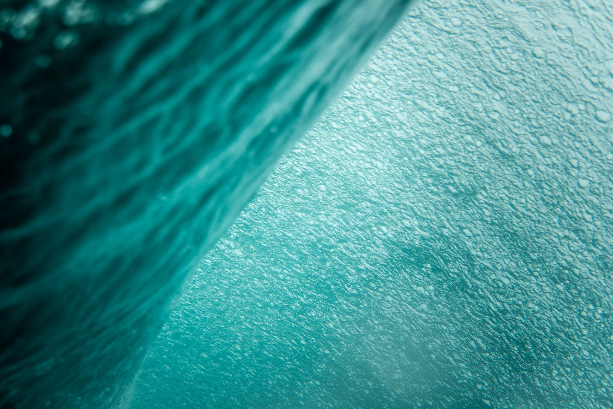 Close-up of a textured turquoise water surface, capturing wave patterns and bubbles.