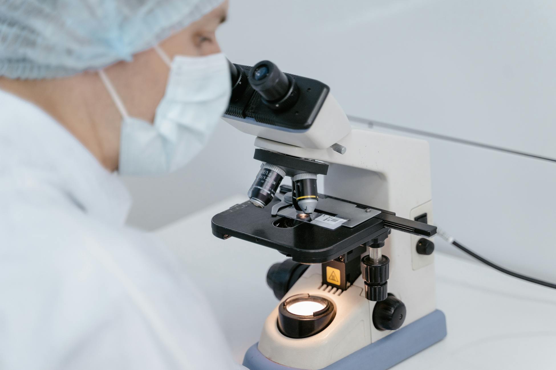Scientist using a microscope in a laboratory setting, wearing protective gear.