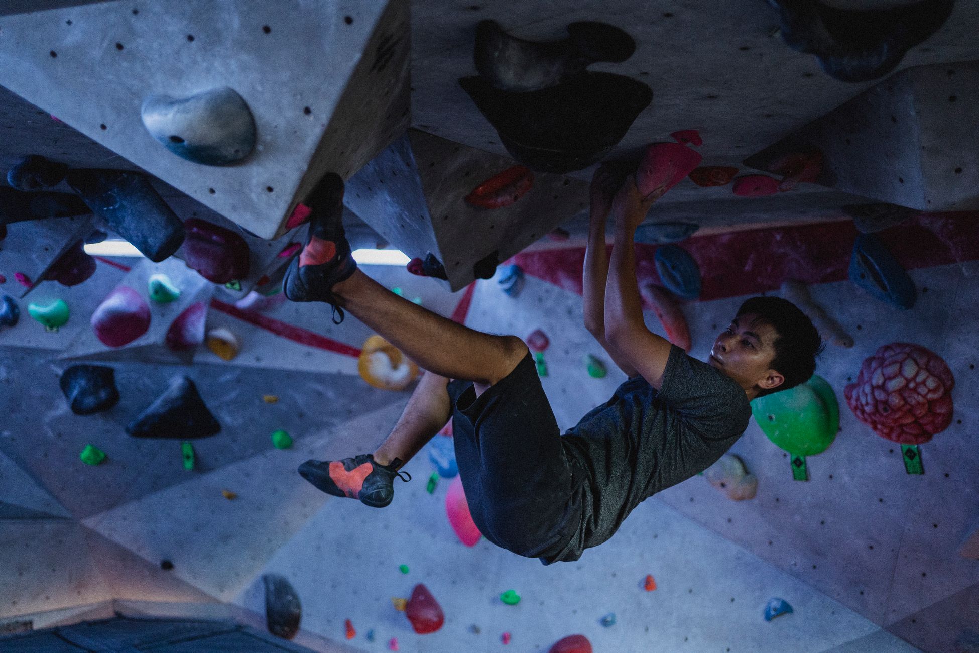 Side view of strong ethnic man practicing on climbing wall in modern bouldering center