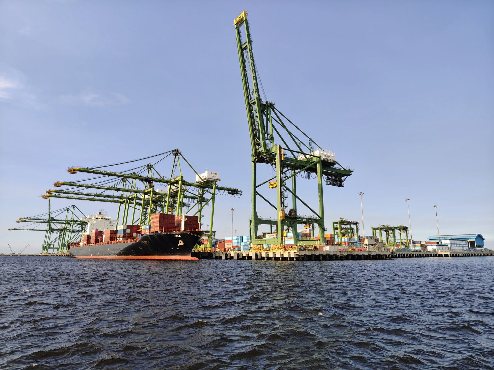 Container ship docked at an industrial port with massive cranes under a clear sky.