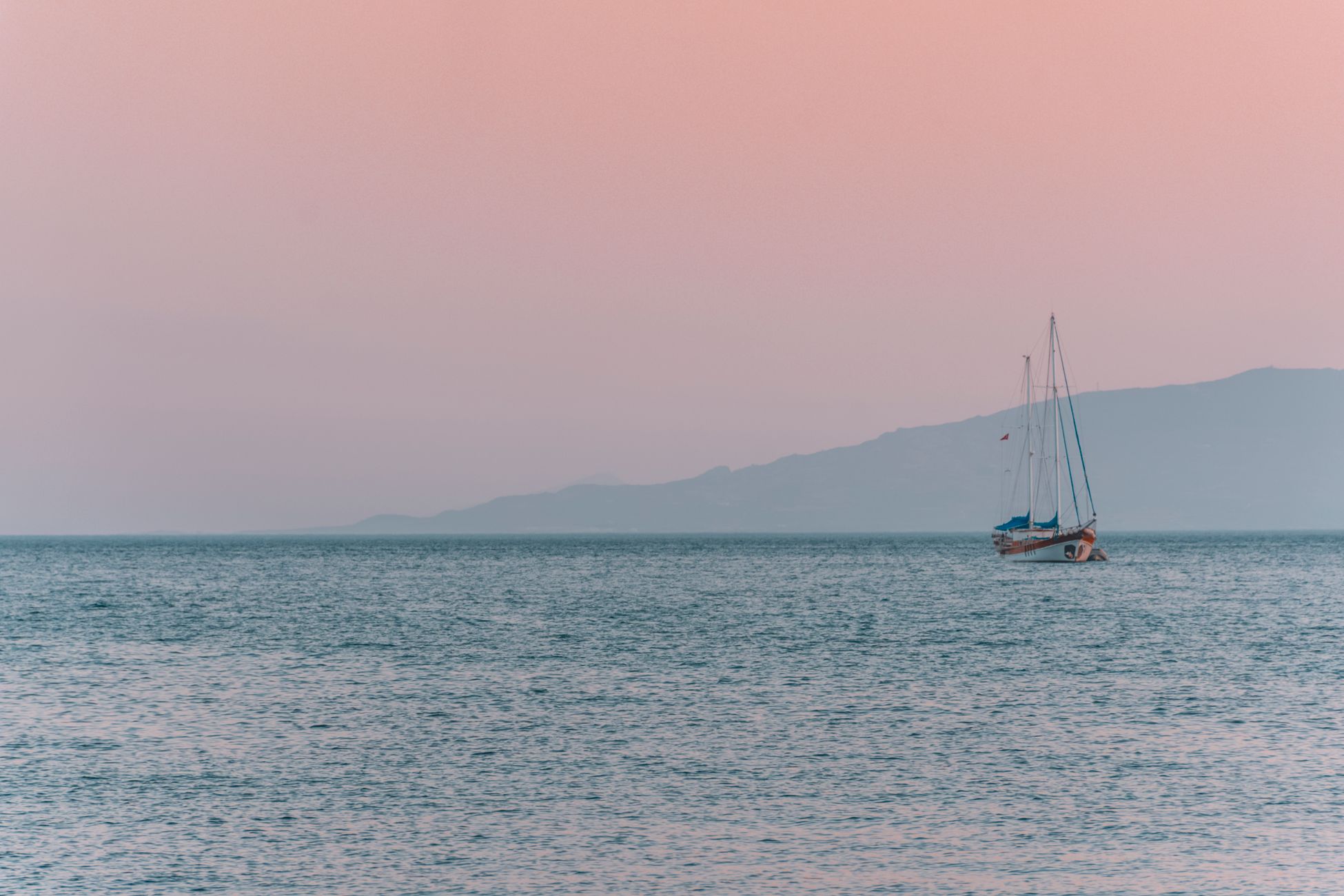 A peaceful sailboat drifts on calm waters during a stunning Turkey sunset.