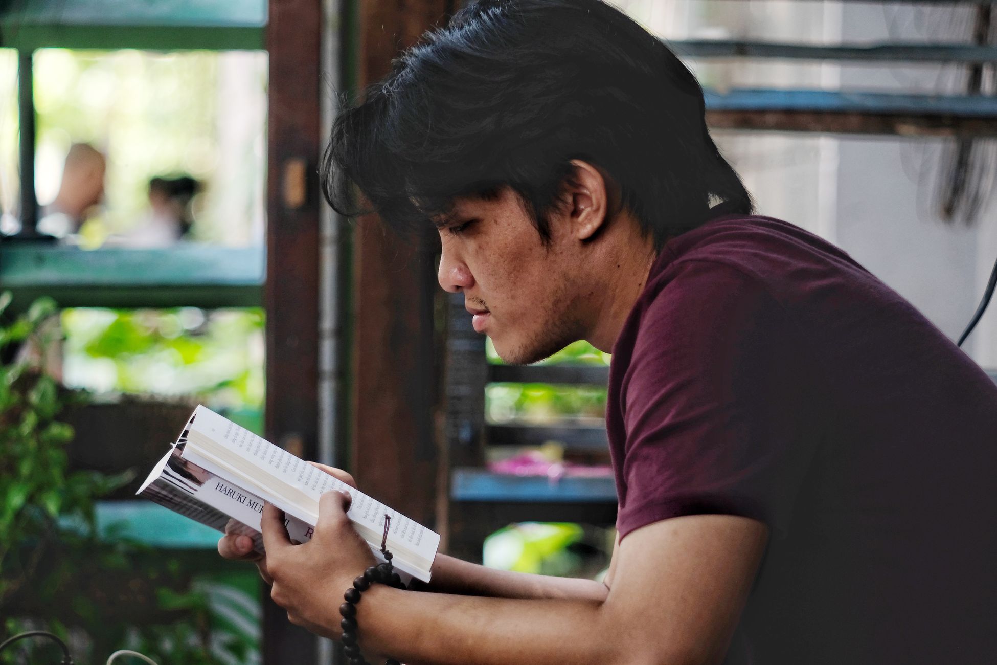 A young man intently reading a book indoors, captured in a relaxed and leisure setting.