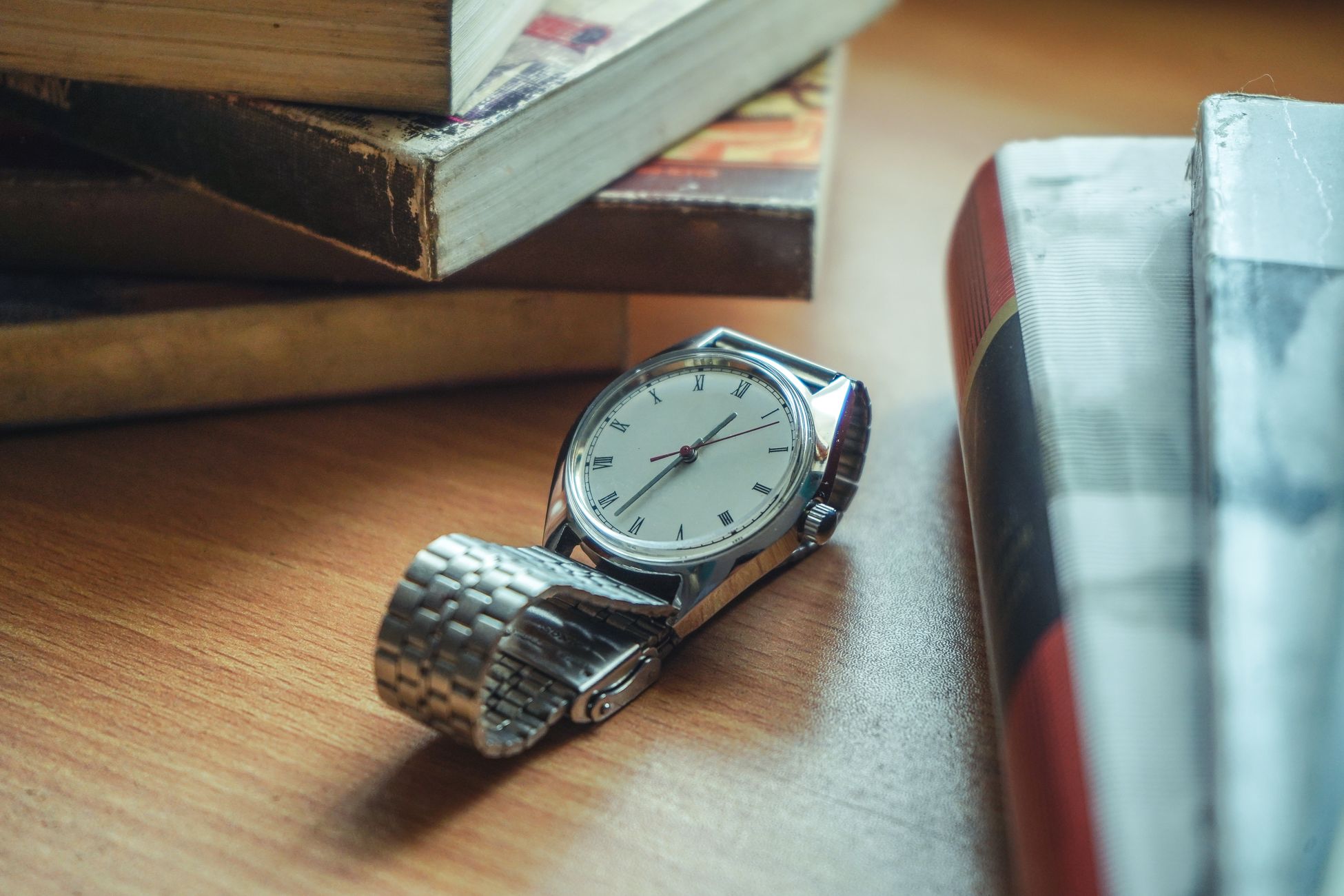 Close-up of a classic analog wristwatch placed on a wooden desk near stacked books.