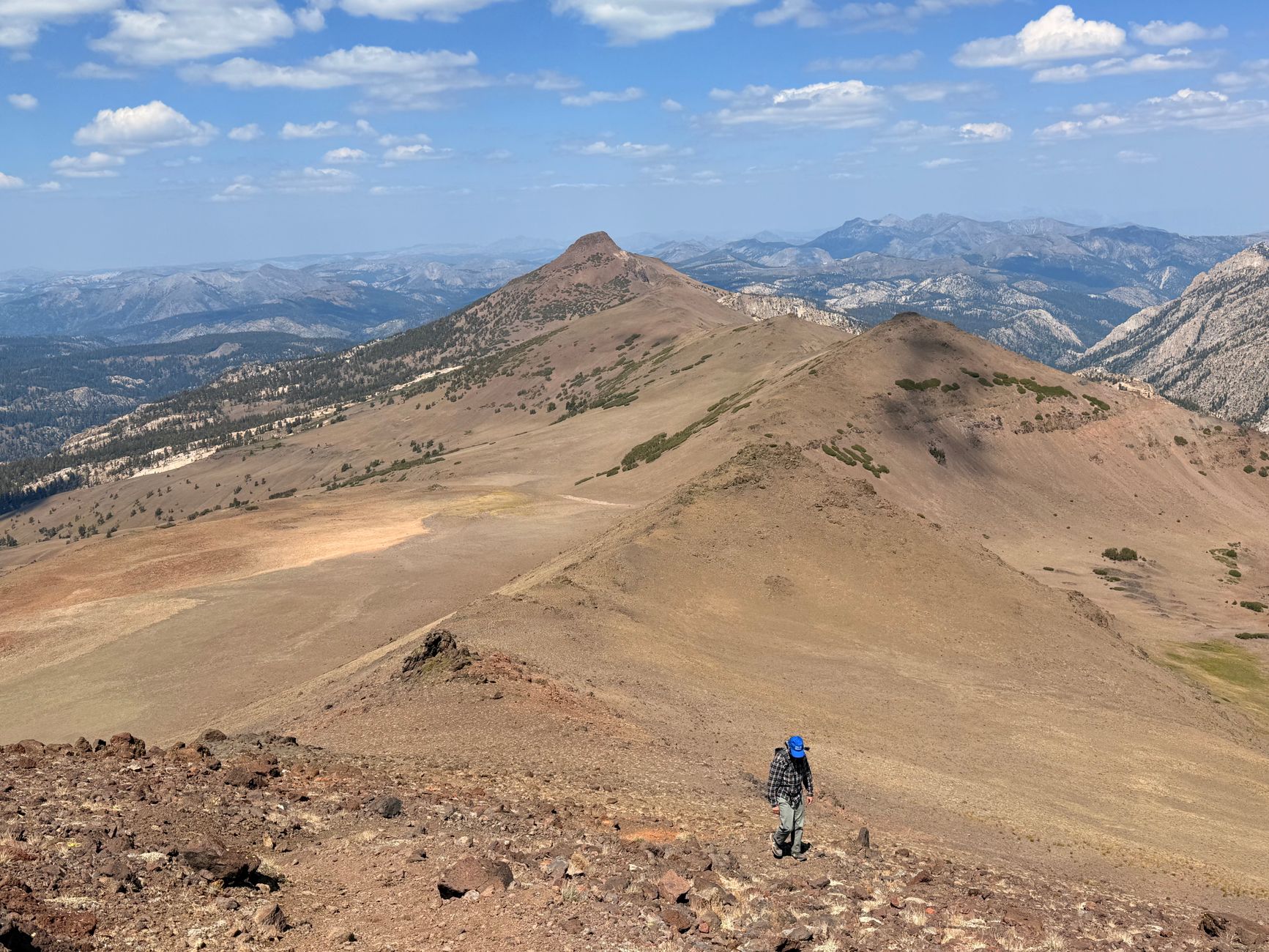 A solitary hiker trekking along the rugged Sierra Nevada mountains under a clear sky.