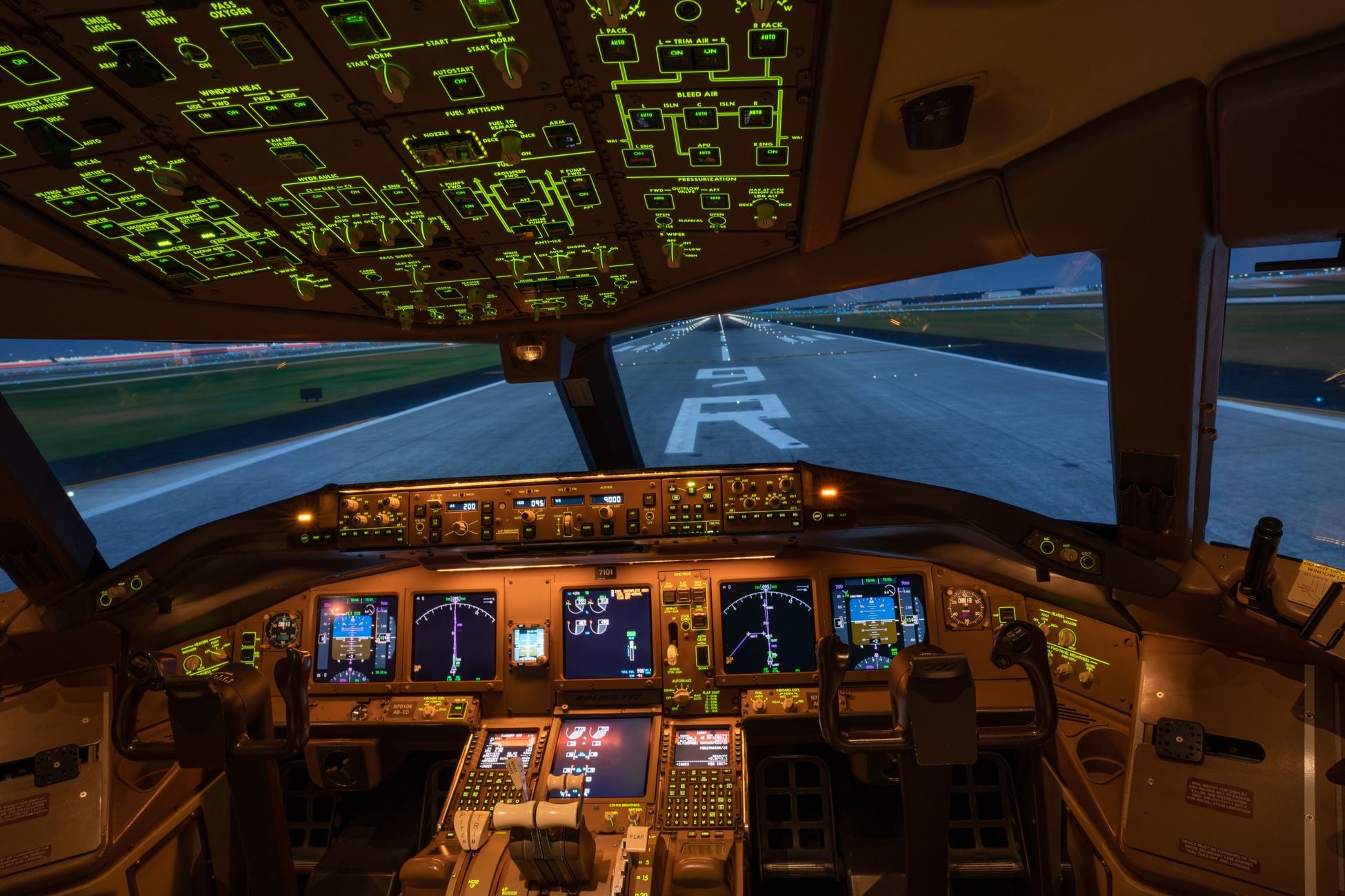 Night view of illuminated airplane cockpit with runway visible, showcasing advanced avionics.