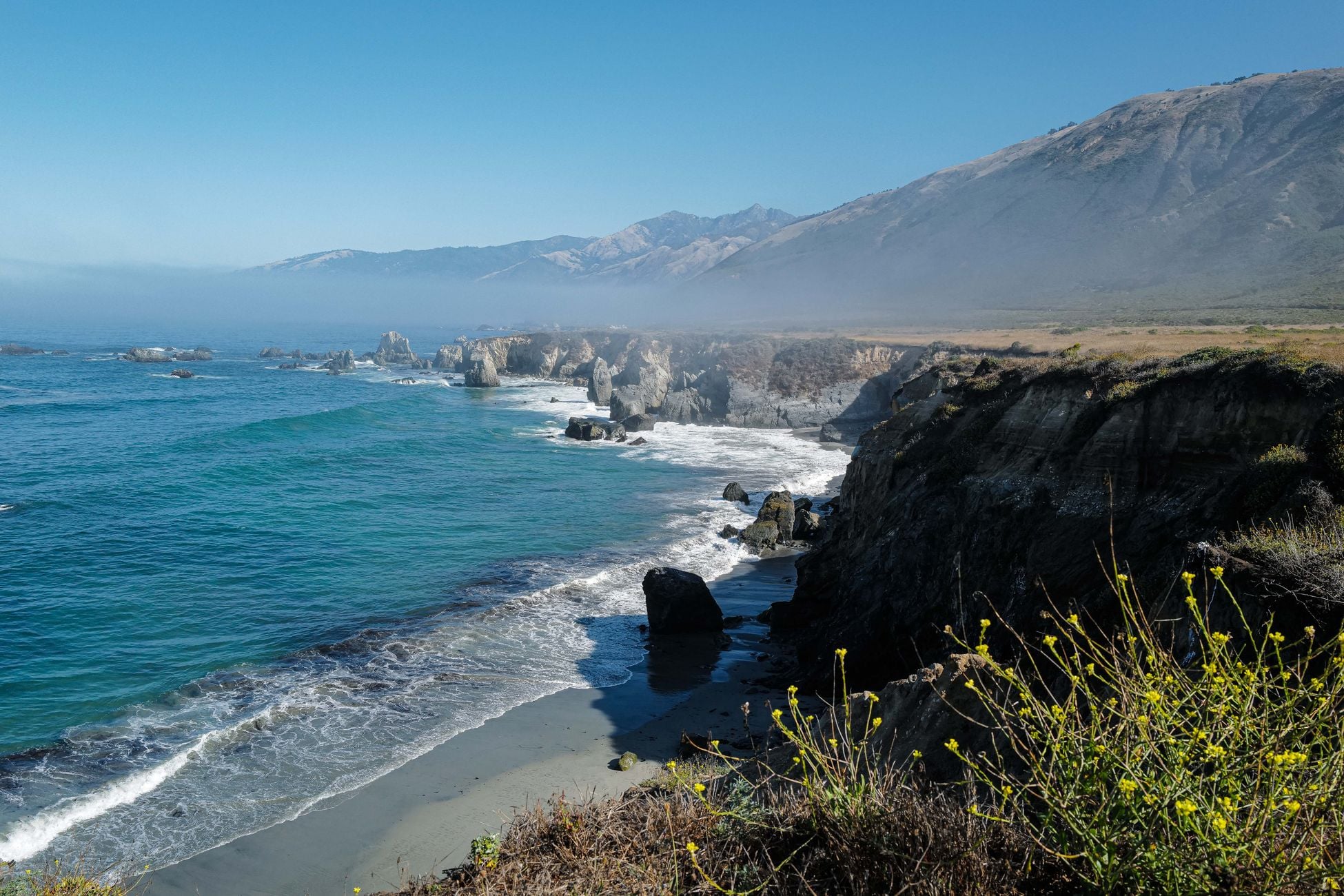Scenic view of the foggy coastline in California with rocky cliffs and blue ocean waves.