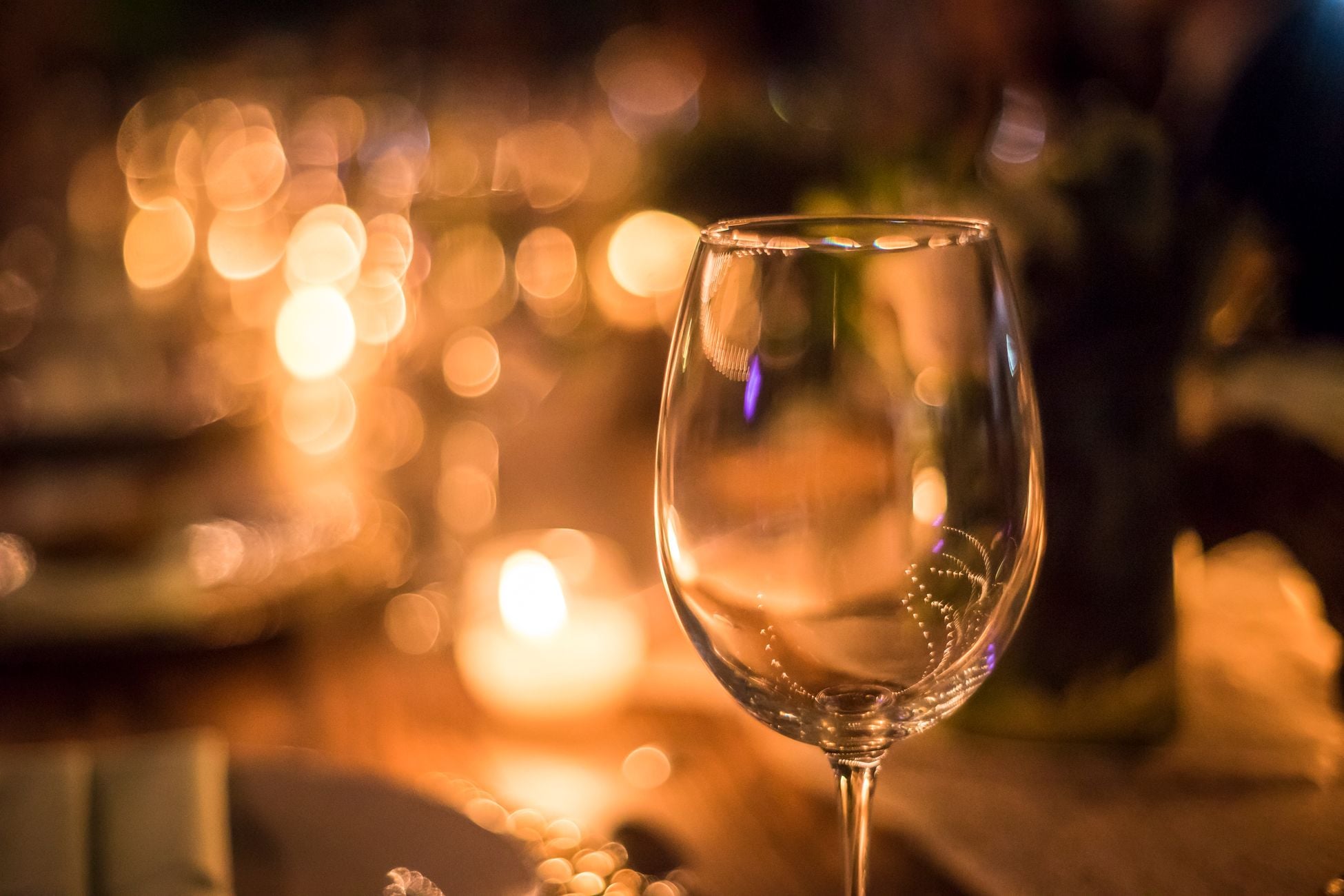 A clear wine glass against a warm, candlelit bokeh background, perfect for elegant dining or festive occasions.