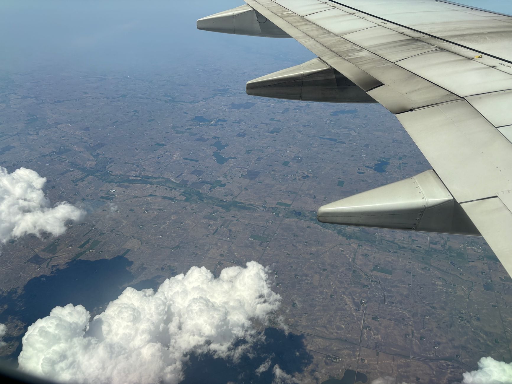 Aerial shot of Minnesota farmland captured from an airplane with clouds below, showcasing agricultural landscape.
