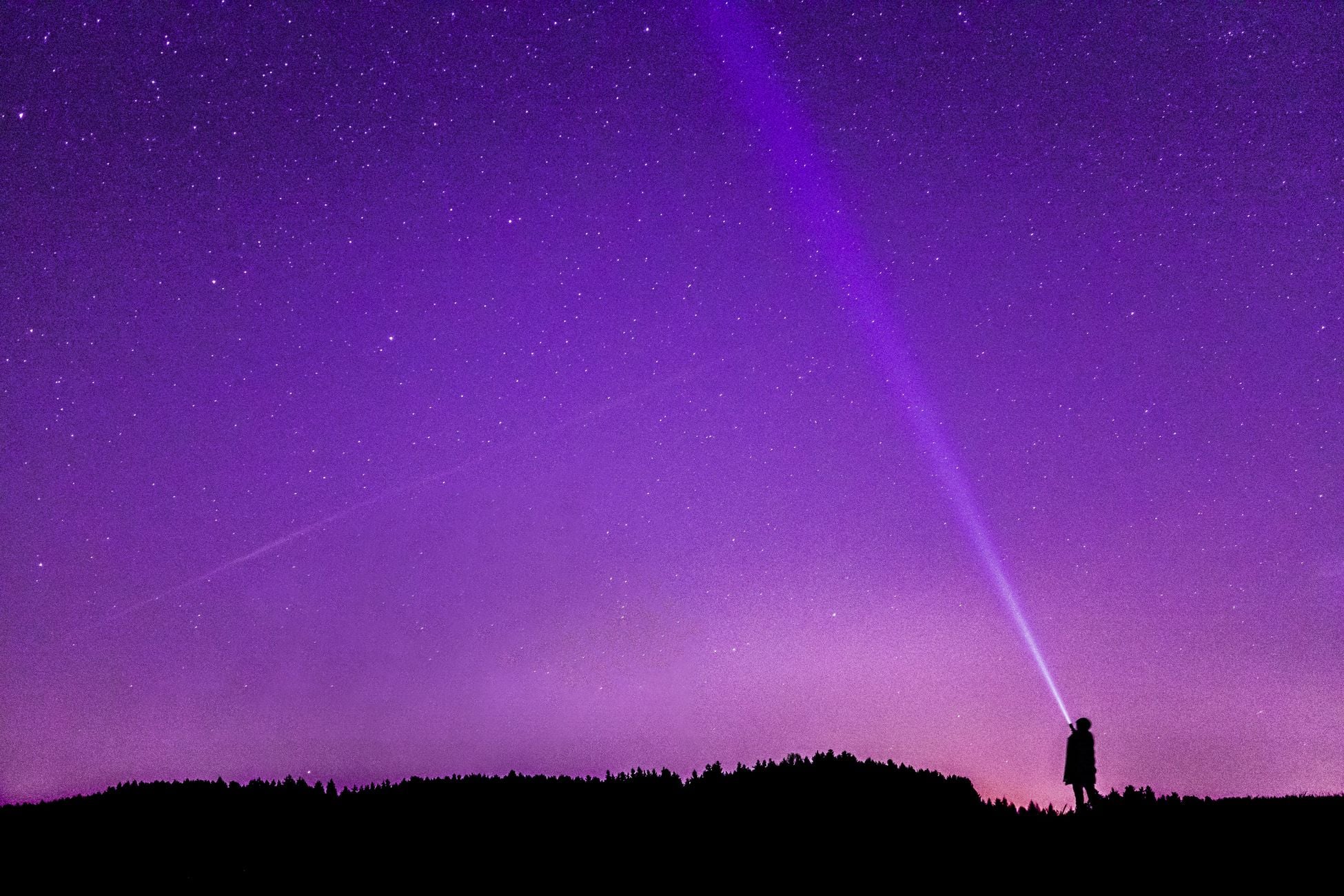 A person with a flashlight standing under a vibrant, starry night sky, highlighting the beauty of space.