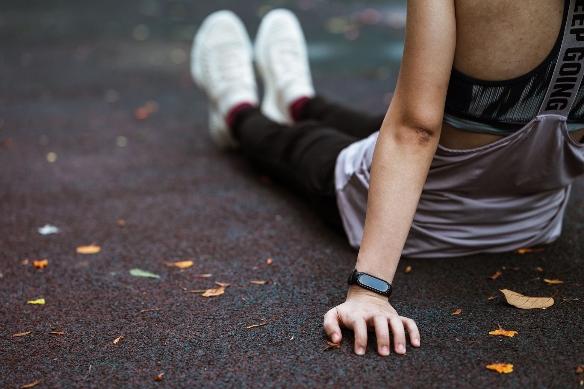 Back view of anonymous female in sportswear and smart watch resting after exercising on sports ground