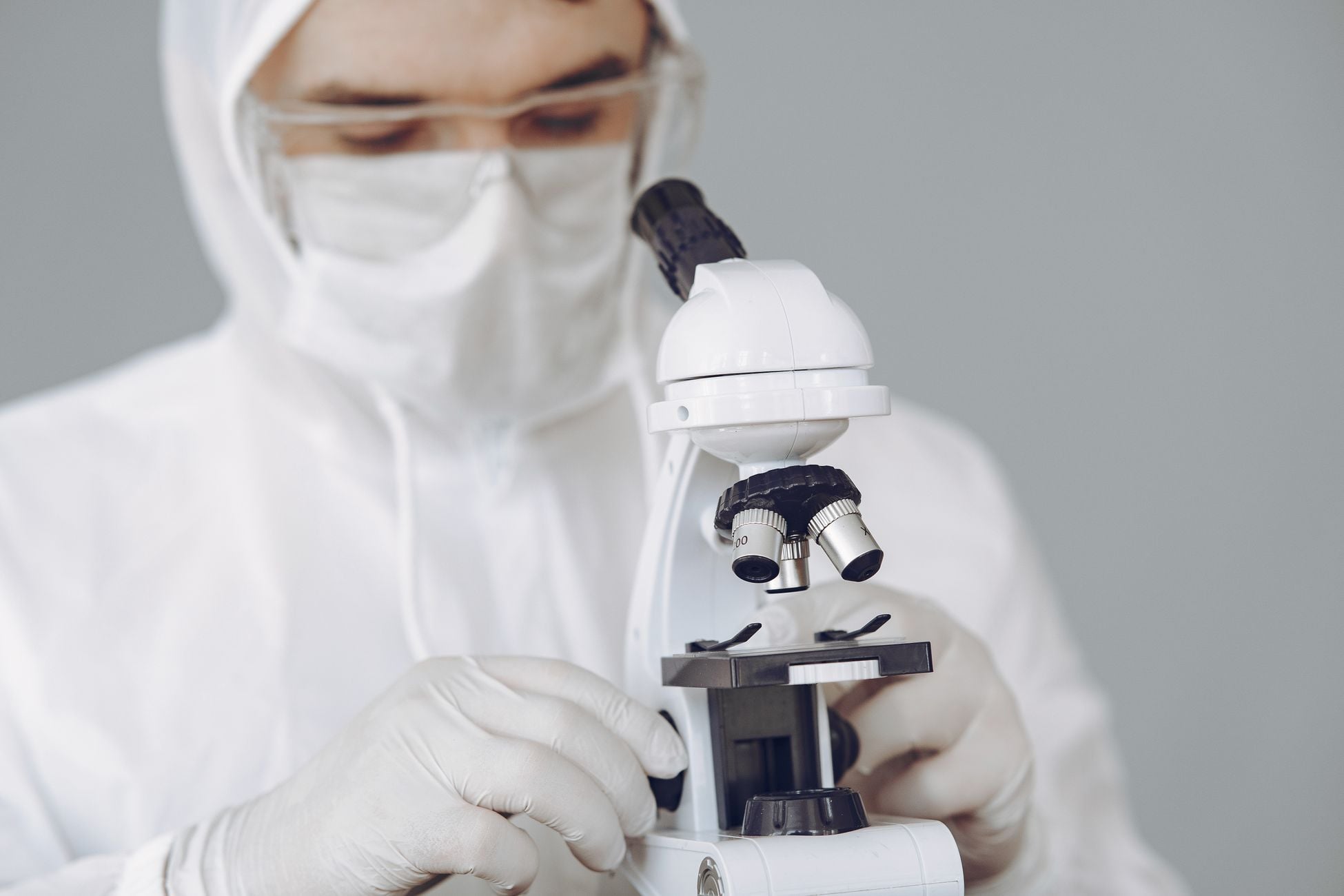 Medical professional in protective gear examining samples with microscope.