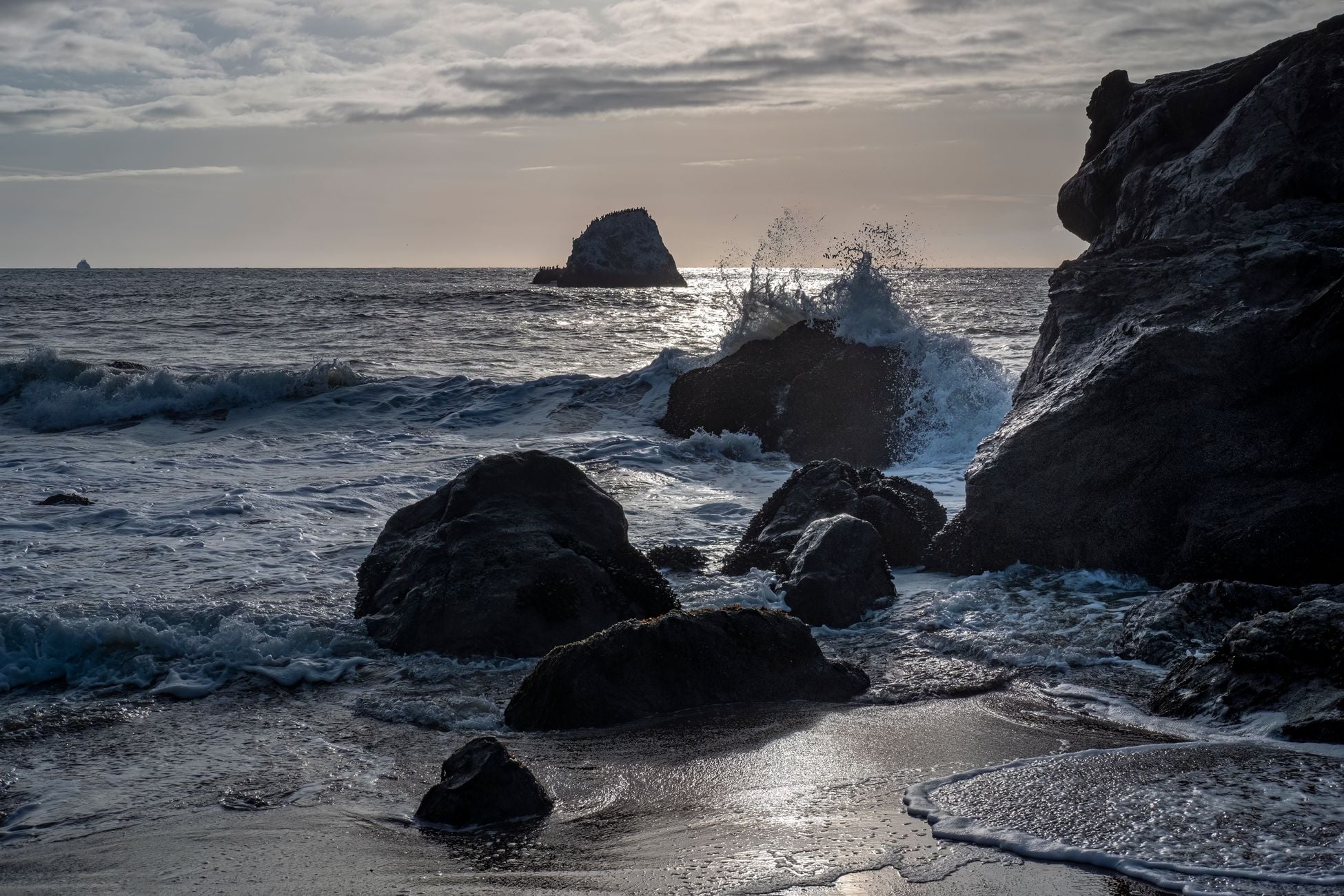 Captivating scene of ocean waves crashing against rocky formations under a cloudy sky.