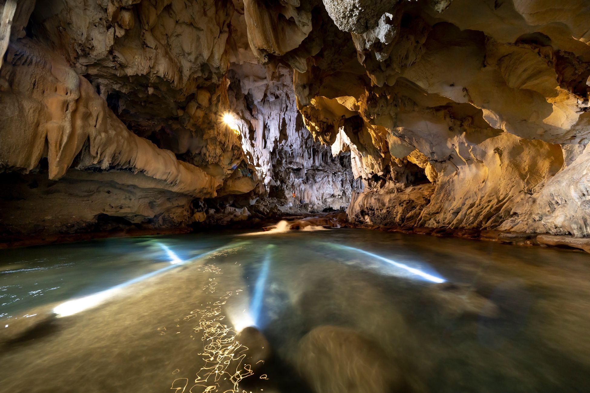 Explore the mystical limestone cave with stunning stalactites and serene water reflections.