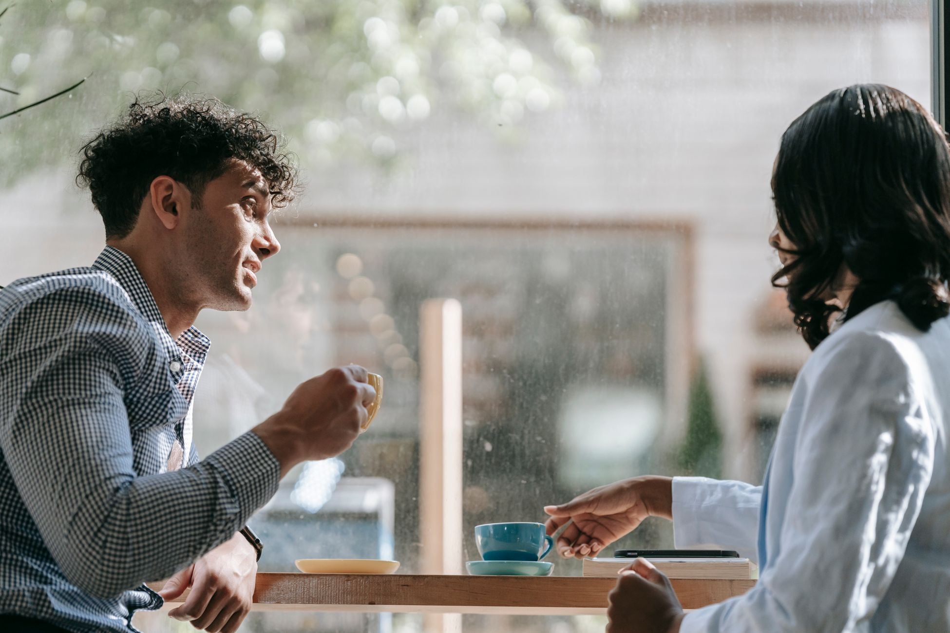 Two adults enjoying a casual conversation over coffee in a cozy café with natural lighting.