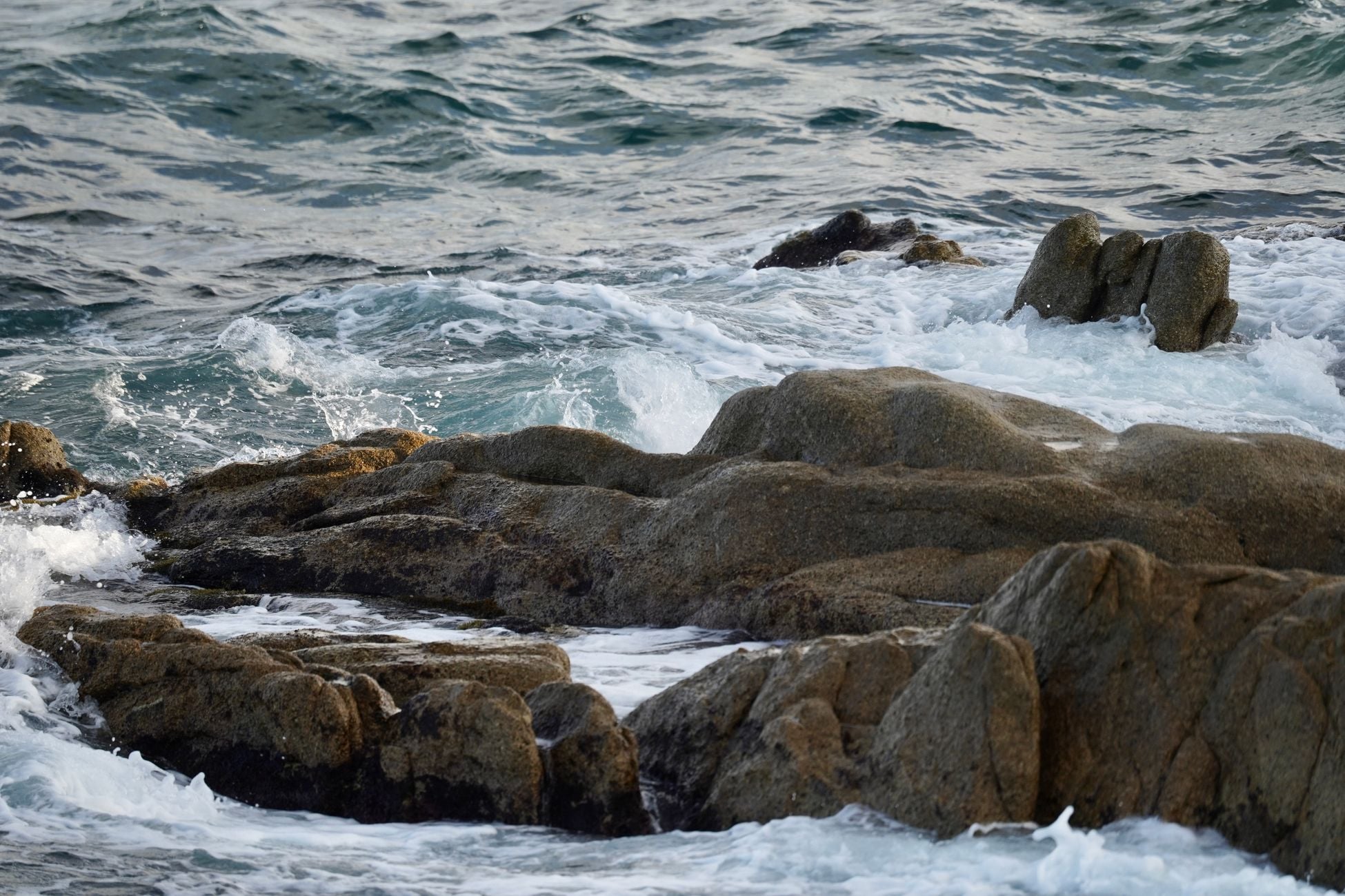 Dramatic waves crash against rugged rocks on a scenic shoreline.