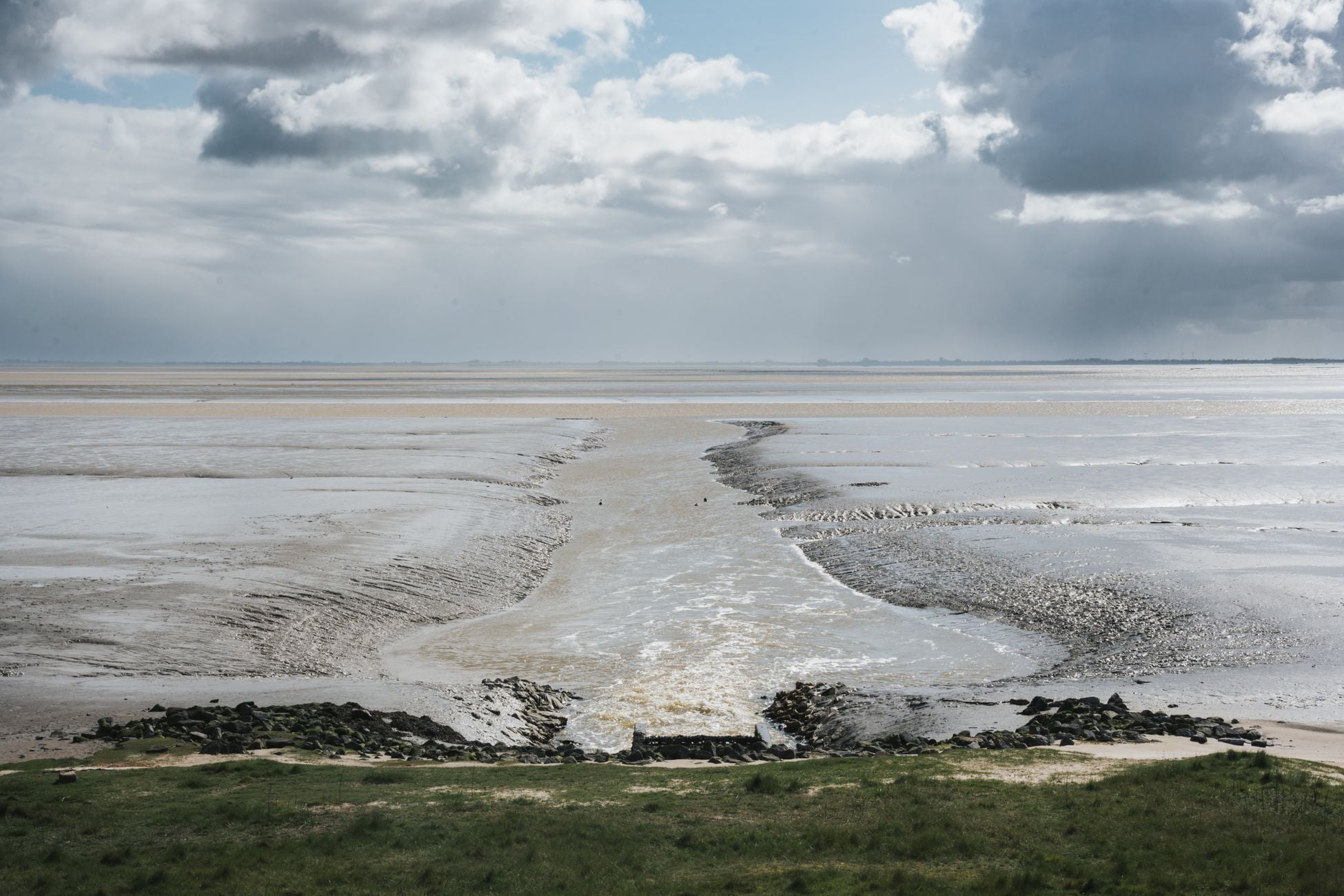 Expansive mudflats merging with the sea under dramatic clouds, showcasing nature's beauty.