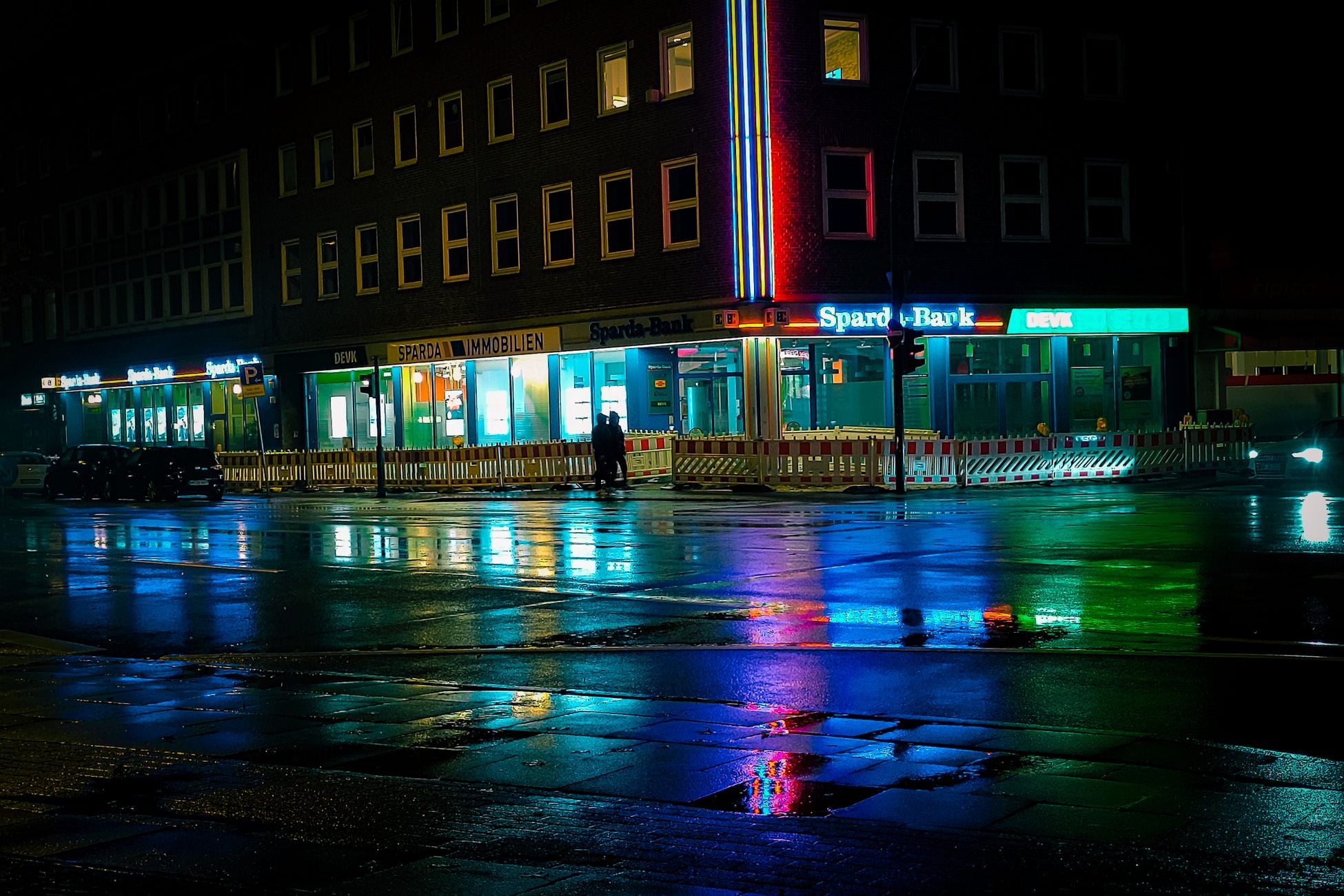 Colorful reflections on wet streets at night in a city with neon lights and building signage.