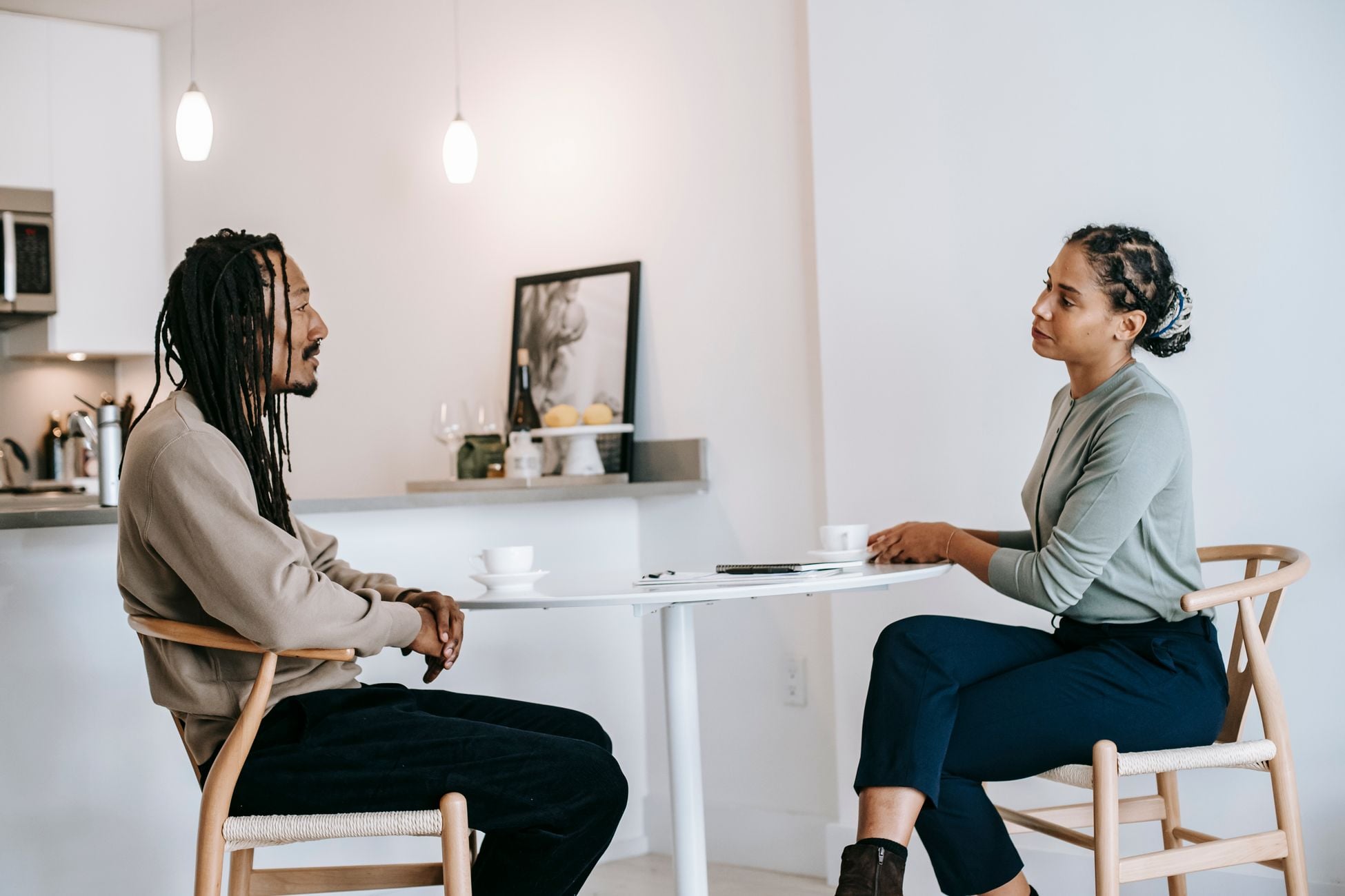 Side view adult African American male in smart casual with dreadlocks answering professional female psychotherapist questions during psychotherapy in light studio