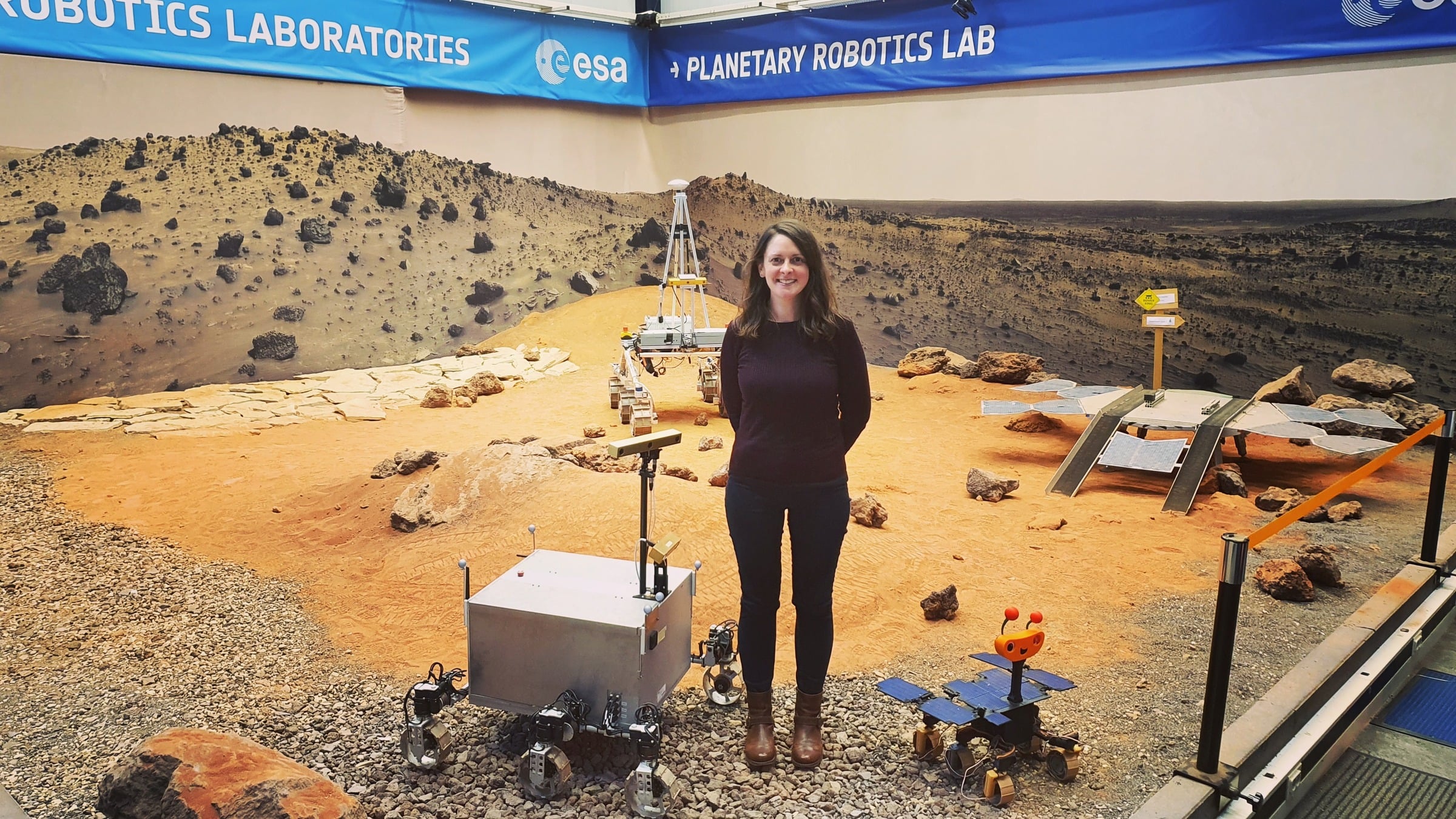 Claire Parfitt standing in ESA Planetary Robotics Lab Mars terrain simulation with rovers