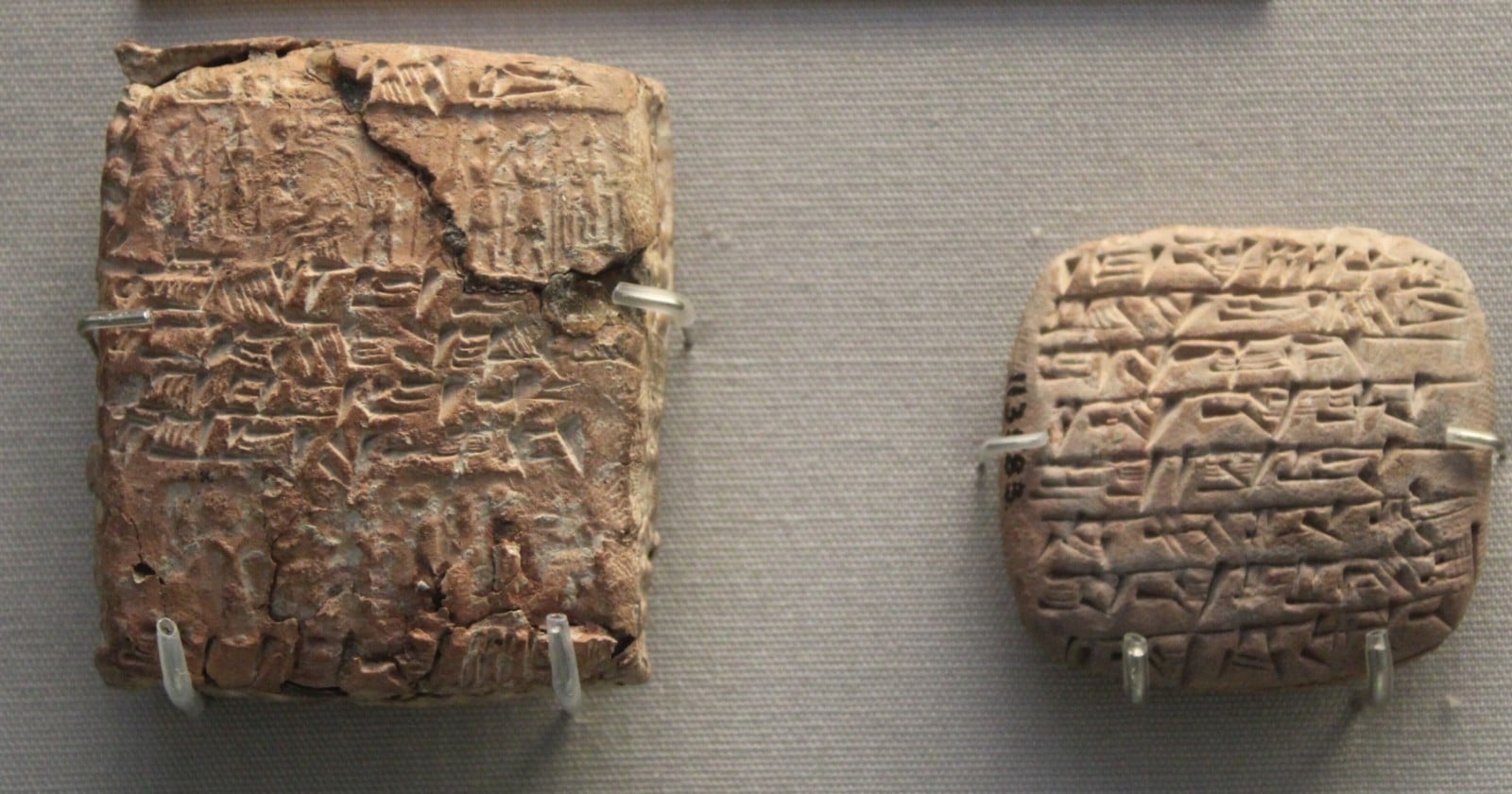 A small clay cuneiform tablet lying beside the clay envelope it was sealed inside, the envelope covered in cylinder-seal impressions.