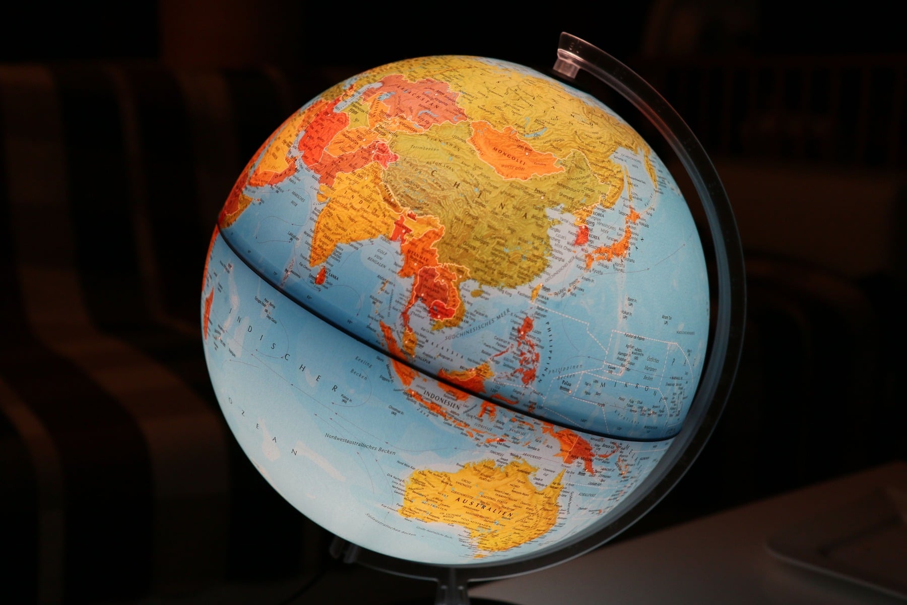 Blue and yellow physical globe showing Asia and Australia against a dark background