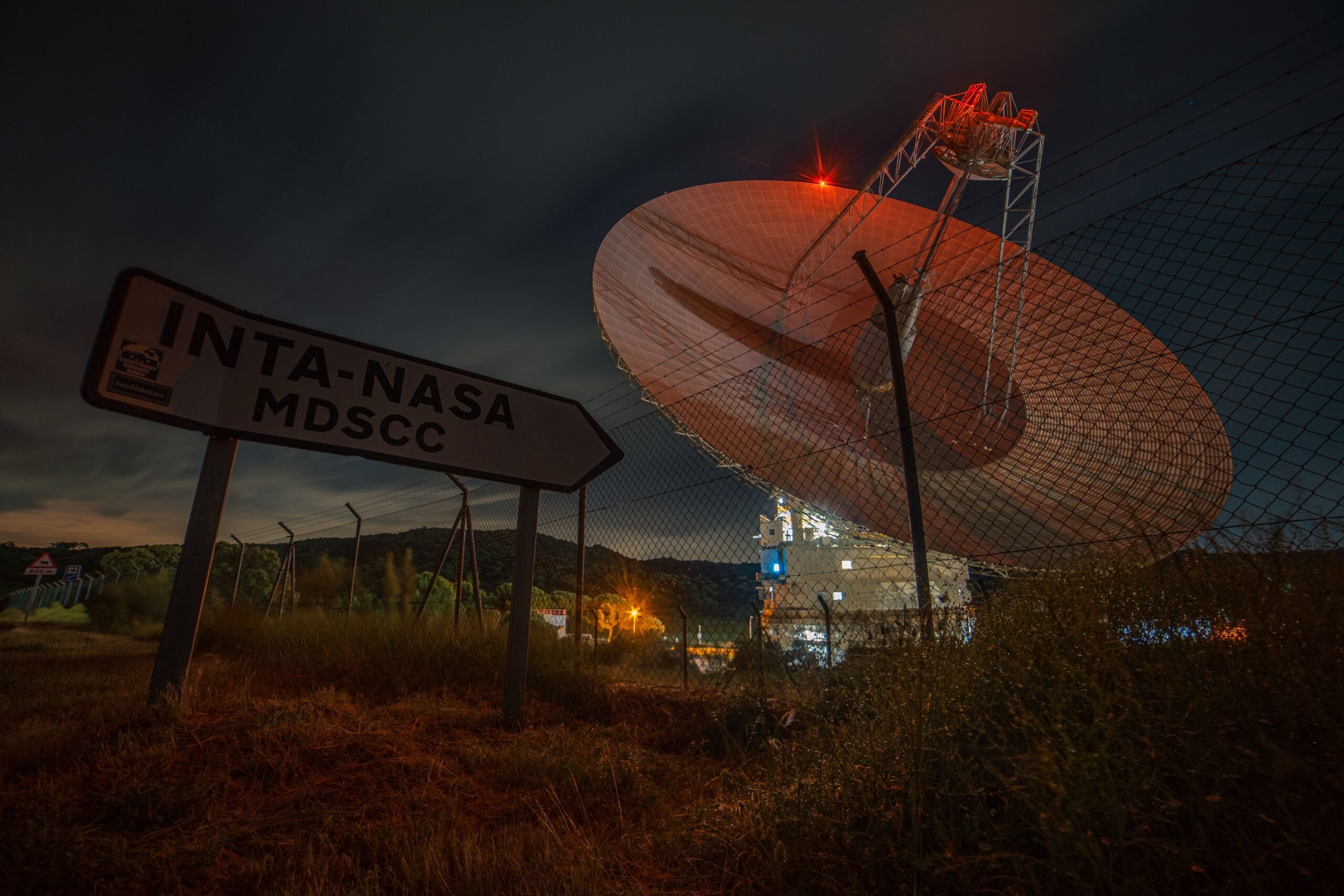 Large radio antenna illuminated at night at Madrid Deep Space Communications Complex