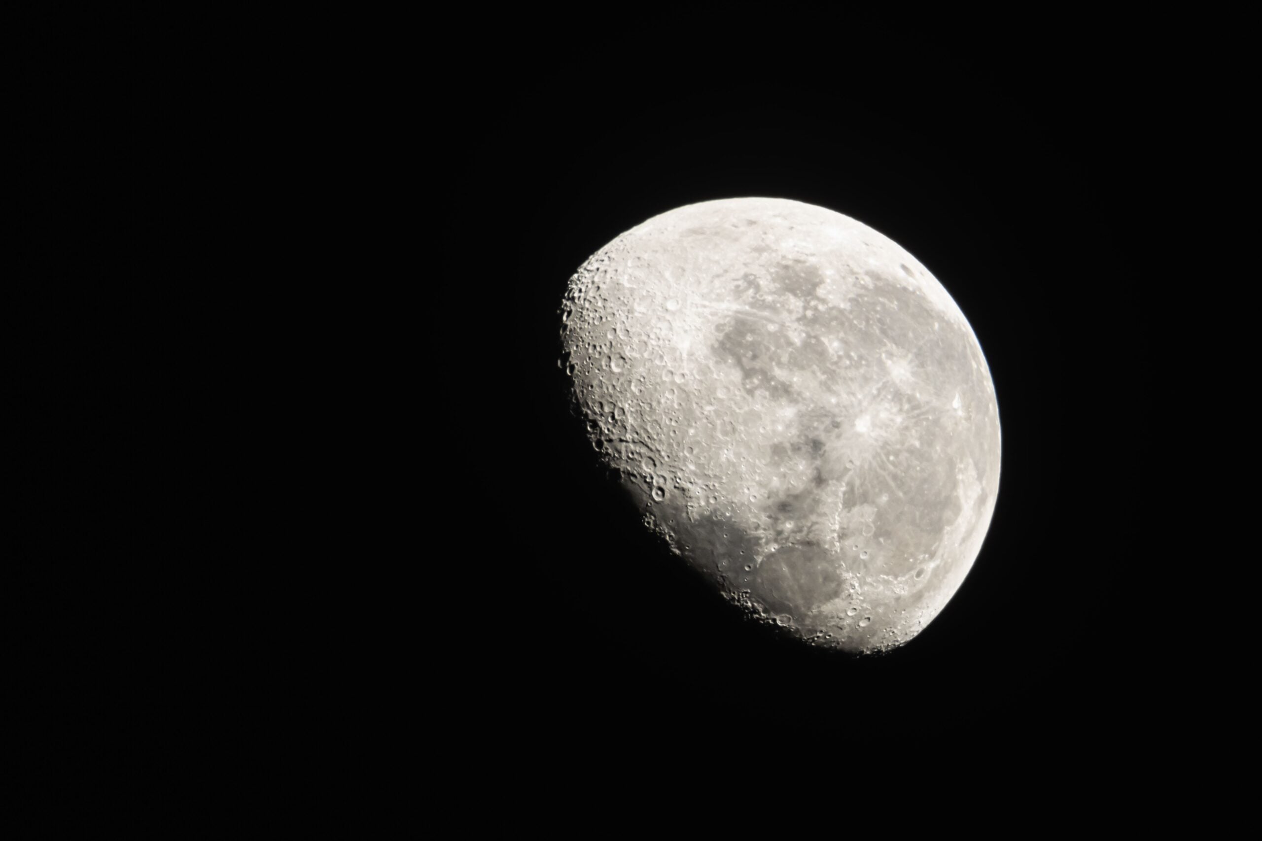 A detailed telescopic photograph of the cratered Moon against a black sky