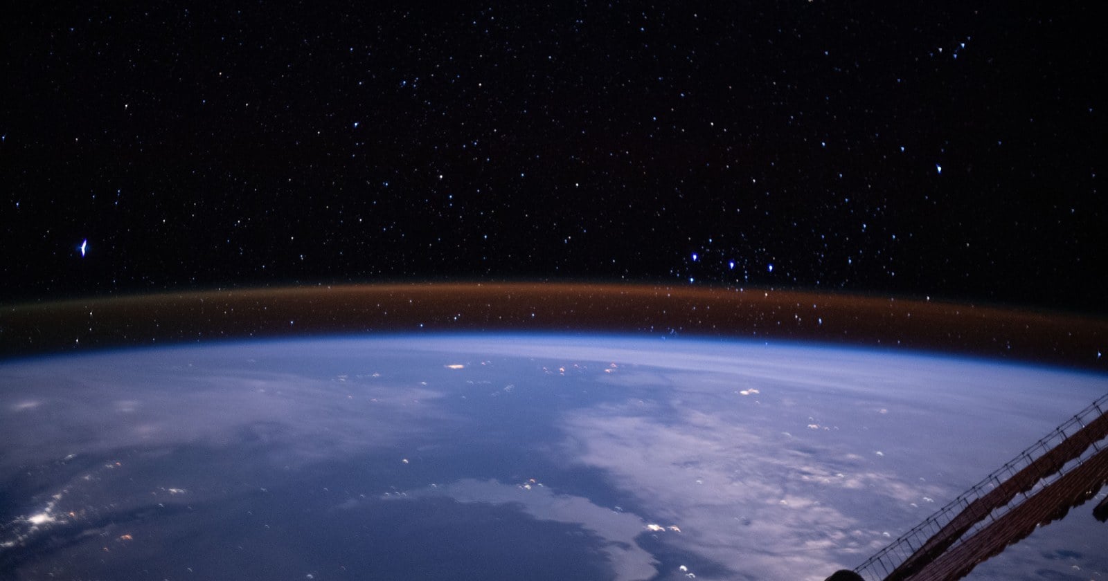 Earth's curved horizon from the International Space Station with a thin amber airglow band above the blue atmosphere and stars behind